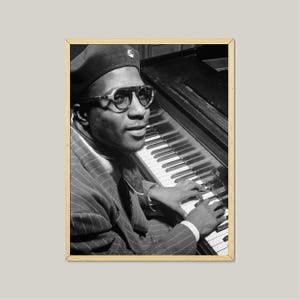 Puede incluir: Fotografía en blanco y negro enmarcada de un hombre tocando el piano. El hombre lleva boina, gafas de sol y un traje de raya diplomática. Sus manos están sobre las teclas del piano. La fotografía está en un marco de madera.