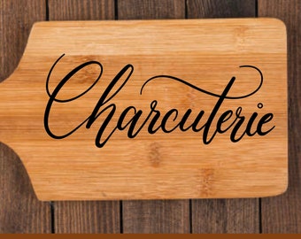 May include: A wooden cutting board with the word "Charcuterie" written in black cursive script.