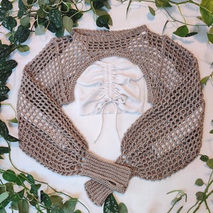 beige crochet sleeves flat lay surrounded by draping leaves, beige crochet bolero, beige shrug