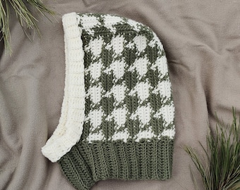 May include: A green and white crocheted hat with a houndstooth pattern. The hat has a long flap that can be pulled over the ears.