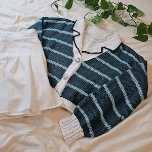 May include: A blue and white striped cardigan with a white collar and white crocheted trim. The cardigan has a button closure and is made of a soft, knitted fabric.