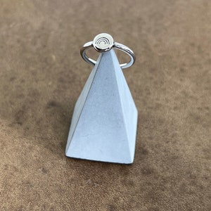 Könnte beinhalten: Ein silberner Ring mit einem kleinen, runden Design, das einen Regenbogen zeigt. Der Ring wird auf einem weißen pyramidenförmigen Ständer präsentiert.