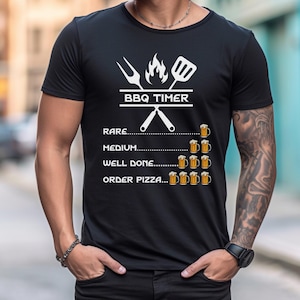 May include: Black t-shirt with a white graphic of a BBQ timer. The timer is a list of doneness levels for meat, with each level represented by a number of beer mugs. The text on the shirt reads "BBQ Timer", "Rare", "Medium", "Well Done", and "Order Pizza".