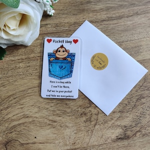 May include: A small plastic card with a pocket hug design. A cartoon monkey is peeking out of a blue jean pocket. The card reads "Pocket Hug" and "Here is a hug while I can't be there, Put me in your pocket and take me everywhere".