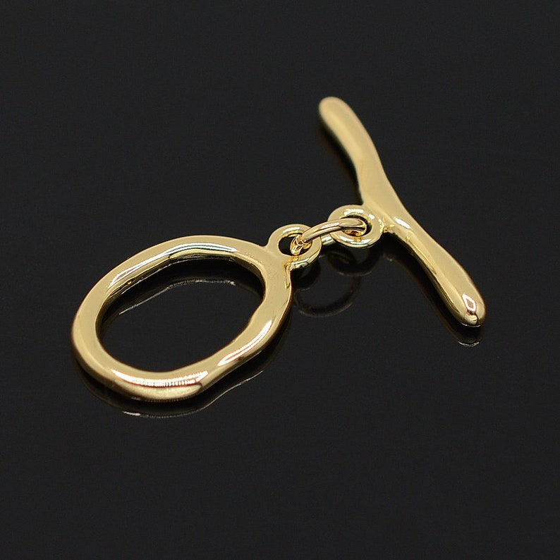 May include: Gold-toned metal toggle clasp with a smooth, rounded oval ring and a straight bar. The clasp is designed for attaching jewelry or other accessories.