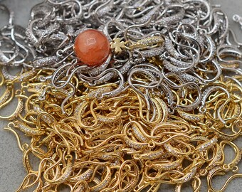 May include: A large pile of gold and silver earring hooks with clear rhinestones. The hooks are arranged in a random pattern and are all the same size and shape.