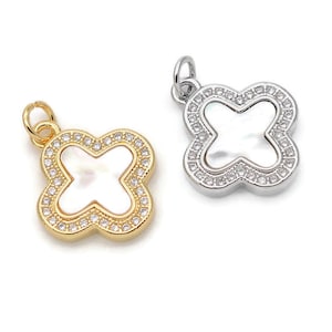 Puede incluir: Dos amuletos de trébol de cuatro hojas en oro y plata con centros de madreperla blanca y detalles de cristal transparente.