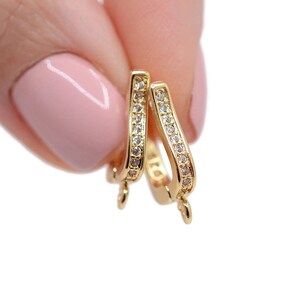 May include: Two gold-toned pendant bails with a row of clear cubic zirconia stones around the edge. Each bail has a loop at the bottom.