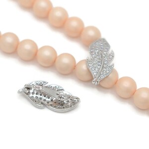 May include: A peach-colored beaded necklace with a silver feather charm. The feather charm is encrusted with clear rhinestones.