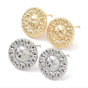 May include: A pair of gold and silver earrings featuring a sun design with a face. The earrings are round and have a textured surface.