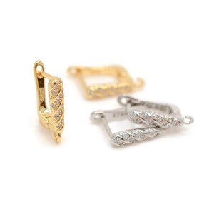 Op de afbeelding: Drie paar oorbellen in goud- en zilverkleuren. De oorbellen hebben een rechthoekige vorm met een gedraaid ontwerp en zijn versierd met kleine, heldere edelstenen. De oorbellen worden gepresenteerd tegen een witte achtergrond.