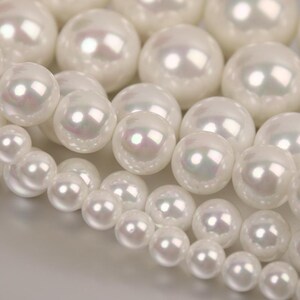 May include: A close-up of a strand of white pearl beads. The pearls are round and smooth, with a slight iridescent sheen.