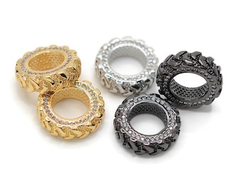 May include: Four tire-shaped charms with a row of clear rhinestones around the edge. The charms are in gold, silver, and black.