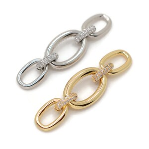 Pode incluir: Dois conectores de corrente, um dourado e outro prateado, com pedras de zirc&ocirc;nia c&uacute;bica transparentes em cada elo.