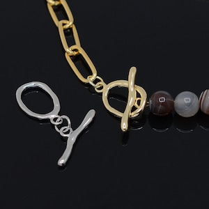 Può includere: Una collana a catena dorata con una chiusura a levetta e perline di agata. Le perline sono un mix di marrone e bianco.