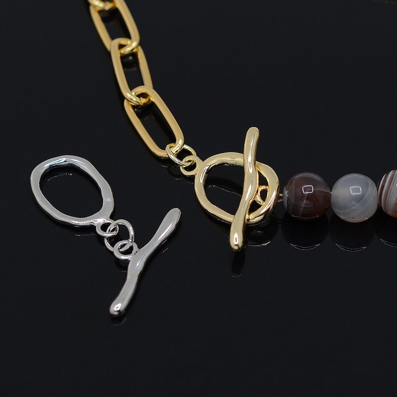 May include: A gold chain necklace with a toggle clasp and agate beads. The beads are a mix of brown and white.
