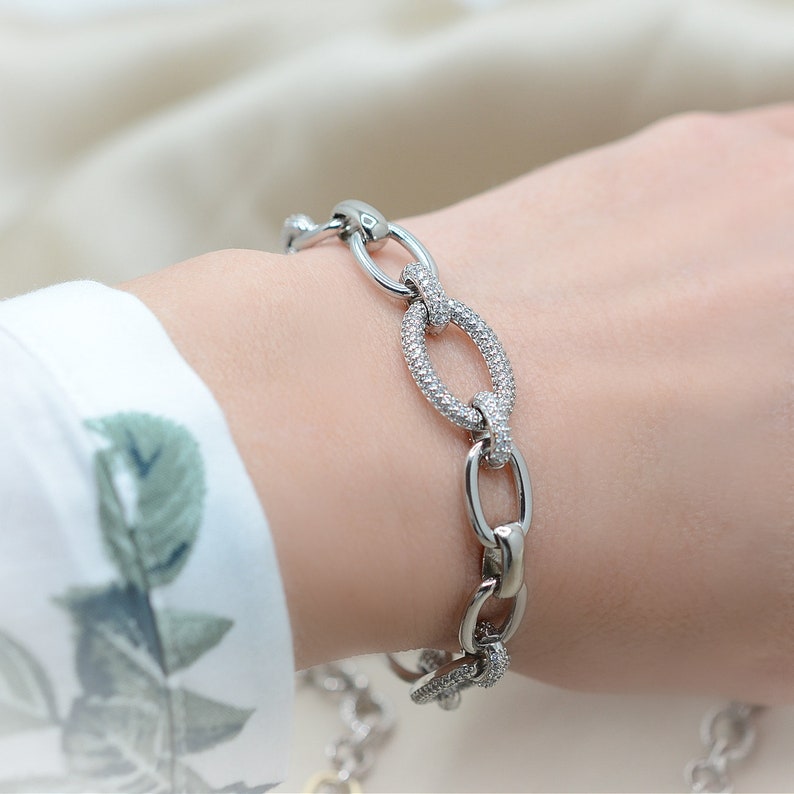 Pode incluir: Um bracelete de prata com elos ovais que s&atilde;o incrustados com pequenas pedras transparentes.