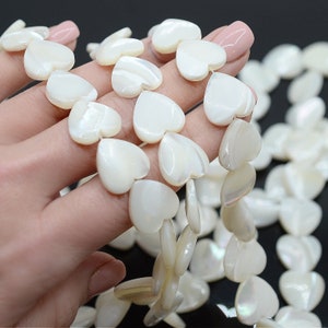 May include: A strand of white mother of pearl heart-shaped beads. The beads are strung on a clear thread and are approximately 1 inch in size.
