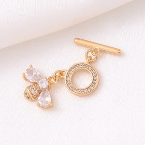 Può includere: Ciondolo dorato con un'ape con accenti di cristallo trasparente e una chiusura a levetta rotonda tempestata di cristalli.