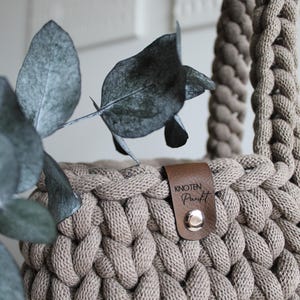 May include: A beige crocheted bag with a brown leather strap and a brown leather tag that says "knoten punkt".