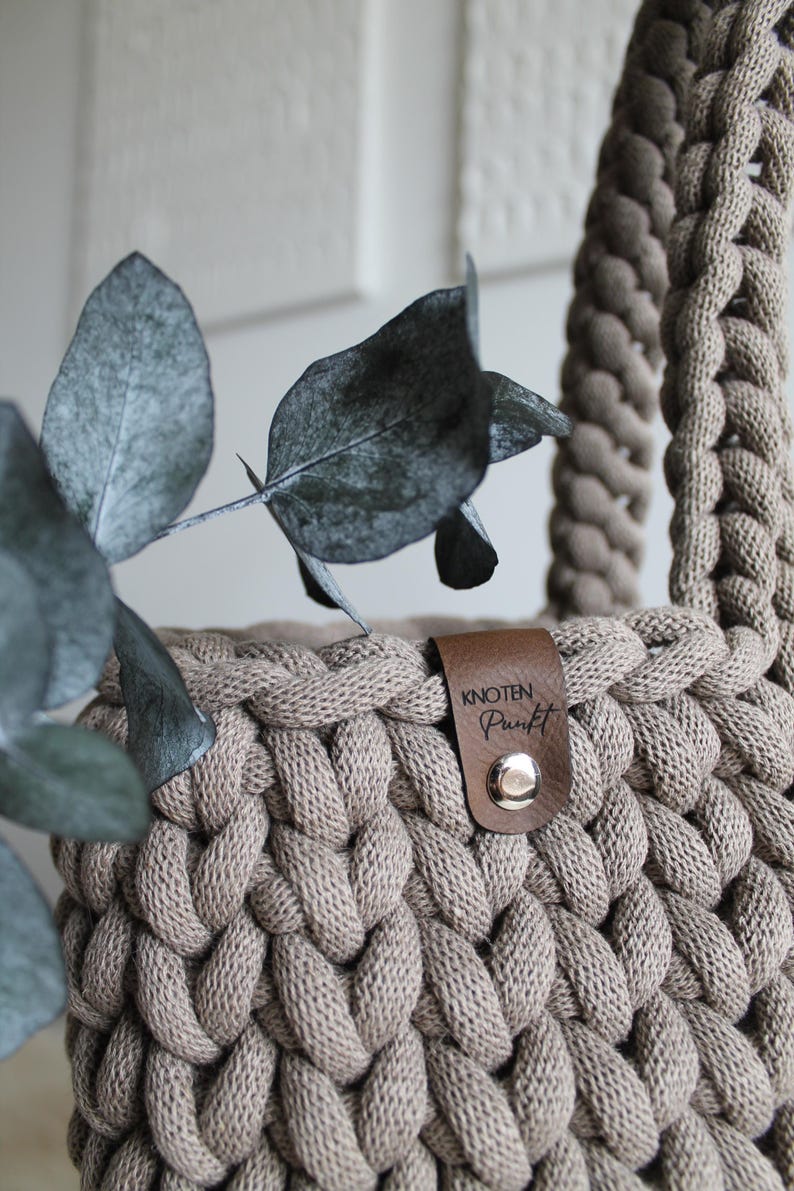 May include: A beige crocheted bag with a brown leather strap and a brown leather tag that says "knoten punkt".