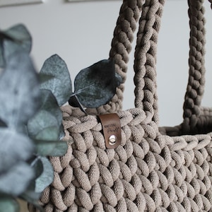 May include: A beige crocheted tote bag with a brown leather tag that says "KNOTEN Punkt".