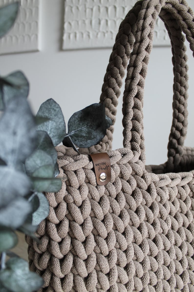 May include: A beige crocheted tote bag with a brown leather tag that says "KNOTEN Punkt".