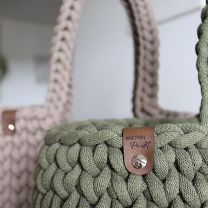 May include: Two crocheted baskets, one in a light brown color and one in a dark green color. The green basket has a brown leather tag with the text "knoten punkt" on it.