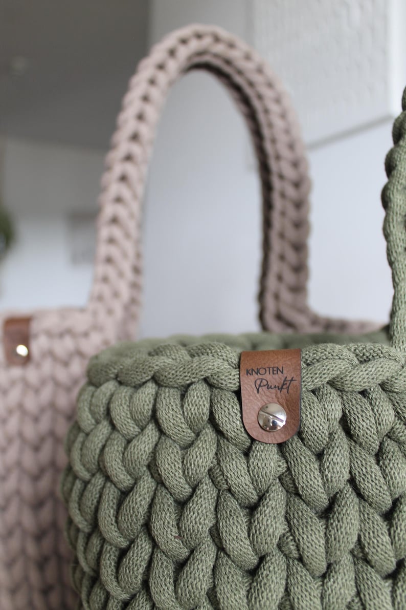 May include: Two crocheted baskets, one in a light brown color and one in a dark green color. The green basket has a brown leather tag with the text "knoten punkt" on it.