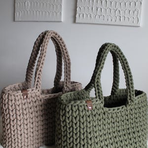 May include: Two crocheted tote bags, one in a light brown color and the other in a dark green color. Both bags have leather handles.