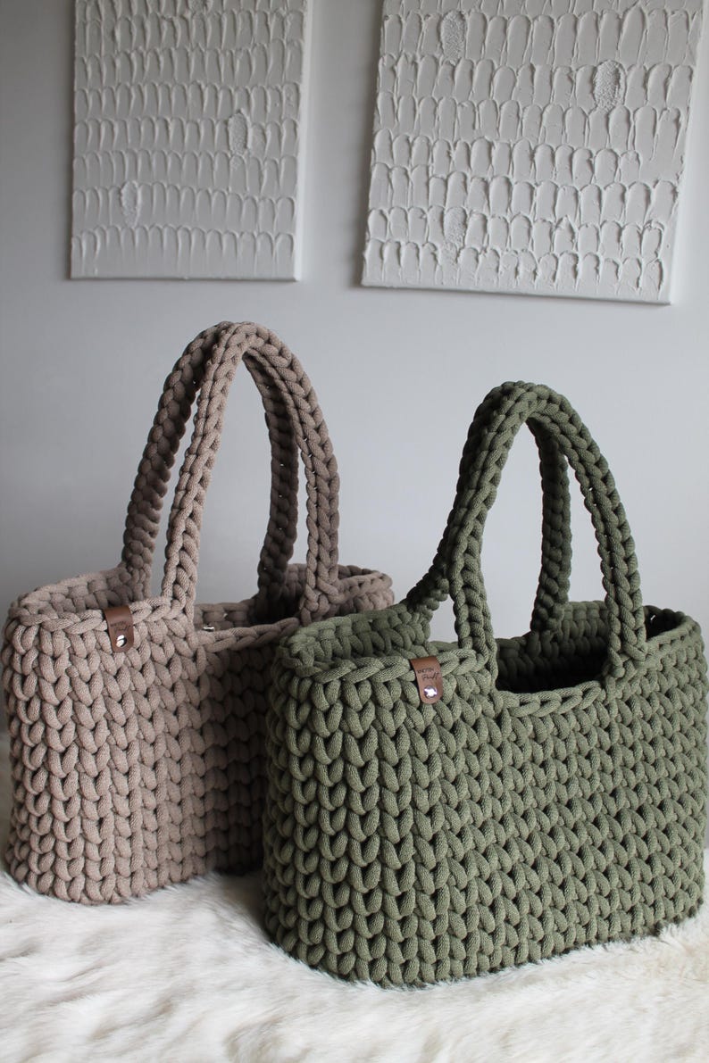 May include: Two crocheted tote bags, one in a light brown color and the other in a dark green color. Both bags have leather handles.