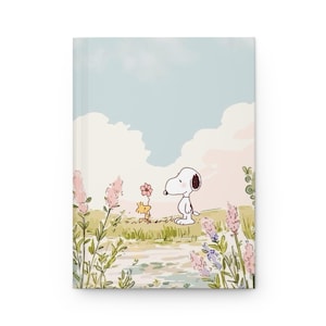 Könnte beinhalten: Ein Hardcover-Notizbuch mit einer skurrilen Illustration von Snoopy und Woodstock in einem Blumenfeld. Das Cover zeigt einen pastellfarbenen Himmel und eine ruhige Landschaft, ideal zum Schreiben und Notizen machen.