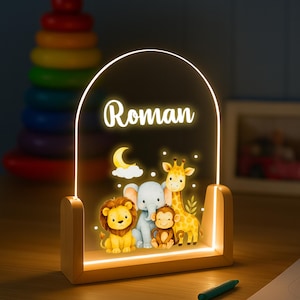 May include: A wooden-based night light with the name "Roman" illuminated in white. The light features a cartoon illustration of a lion, elephant, monkey, and giraffe. A crescent moon and stars are also depicted.