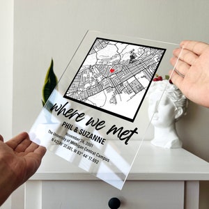 Puede incluir: Un letrero de acr&iacute;lico transparente con el texto "where we met" en escritura cursiva negra. Debajo del texto est&aacute; el nombre "Phil & Suzanne" y la fecha "November 24, 2001". El letrero tambi&eacute;n incluye el texto "The University of Michigan Central Campus" y las coordenadas "N 42&deg; 16' 37.681, W 83&deg; 44' 17.692". Un mapa en blanco y negro con un punto rojo que marca una ubicaci&oacute;n est&aacute; en la esquina superior derecha del letrero.