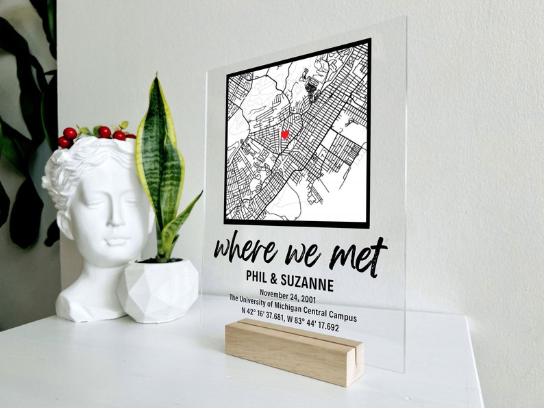Puede incluir: Un letrero de acr&iacute;lico transparente con texto negro y un mapa en blanco y negro. El texto dice "where we met", "Phil & Suzanne", "November 24, 2001", "The University of Michigan Central Campus", y "N 42&deg; 15' 37.681, W 83&deg; 44' 17.692". Un coraz&oacute;n rojo est&aacute; marcado en el mapa.