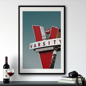 May include: A framed print of a red and white sign with the text "The Varsity" and "Eat, Sleep, Love The Varsity Since 1928". The sign is against a blue sky.