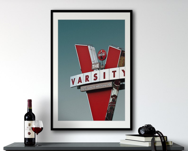 May include: A framed print of a red and white sign with the text "The Varsity" and "Eat, Sleep, Love The Varsity Since 1928". The sign is against a blue sky.