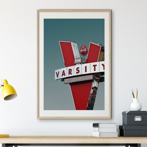 May include: A framed photograph of a red and white sign with the words "The Varsity" and "Serving the Varsity Since 1929". A Coca-Cola logo is visible on the sign.