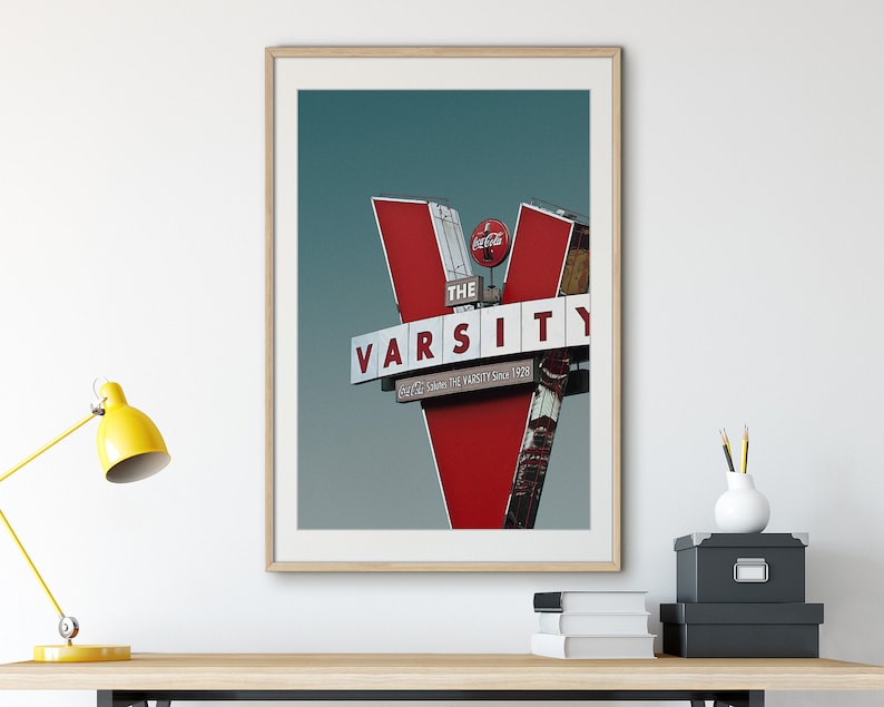 May include: A framed photograph of a red and white sign with the words "The Varsity" and "Serving the Varsity Since 1929". A Coca-Cola logo is visible on the sign.