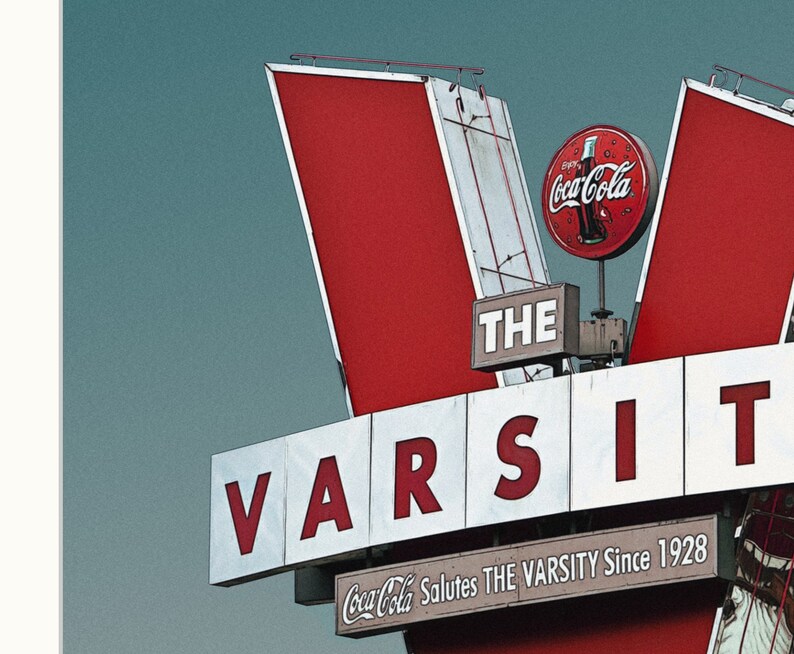 May include: A red and white sign with the words "THE VARSITY" in large white letters. The sign also features a red Coca-Cola logo and the text "Coca-Cola Salutes THE VARSITY Since 1928".
