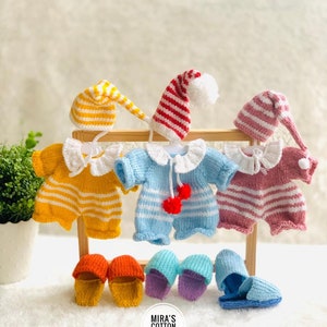Può includere: Un assortimento di vestiti e accessori per bambole fatti a mano. Il set include tutine a righe gialle, blu e rosa con colletti bianchi, cuffie da notte abbinate e pantofole. Il testo "Mira's Cotton Friends" è visibile.