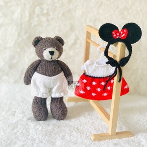 K&ouml;nnte beinhalten: Ein brauner, gestrickter Teddyb&auml;r mit wei&szlig;en Shorts steht neben einem Holzst&auml;nder mit einem rot-wei&szlig; gepunkteten Kleid und schwarzen M&auml;useohren mit roter Schleife. Der Text "Mira's Cotton Friends" ist sichtbar.