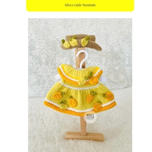 May include: A yellow knitted outfit and hat set with lemon appliqués. The dress has a white trim and is displayed on a wooden hanger. The hat is brown with yellow lemon accents. Text on the image reads "Little Lemon Outfit & Hat" and "Mira's Little Wardrobe."