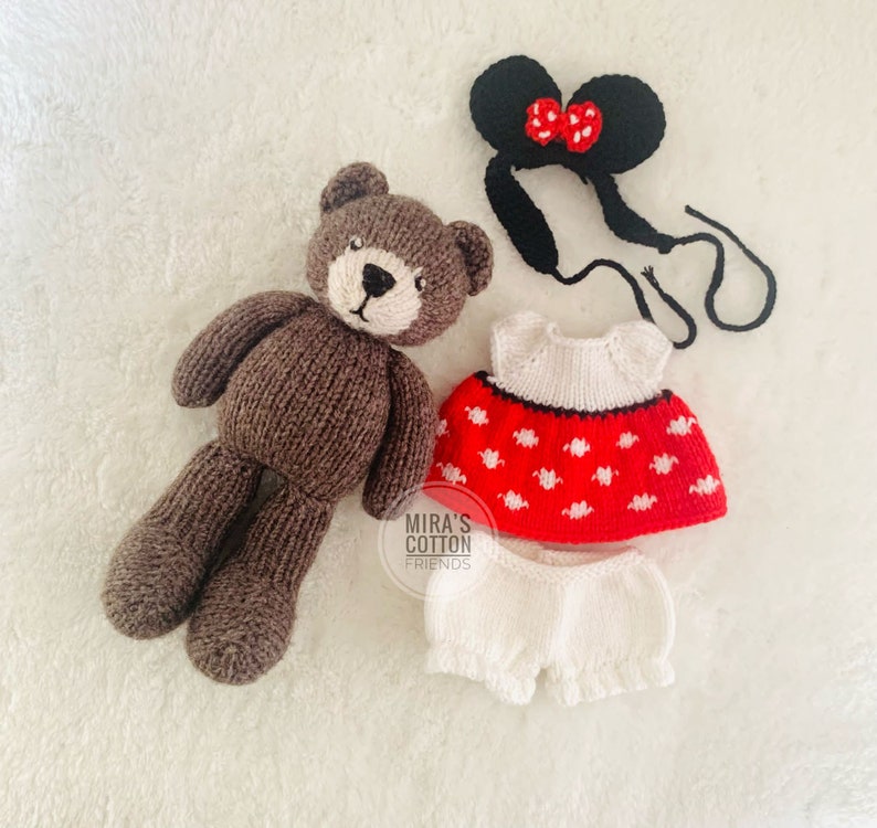 K&ouml;nnte beinhalten: Ein gestrickter brauner Teddyb&auml;r mit wei&szlig;er Schnauze und passendem Outfit. Das Outfit umfasst ein rotes Kleid mit wei&szlig;en Punkten, wei&szlig;e Pumphosen und ein schwarzes Stirnband mit roter Schleife. Die Artikel liegen auf einer wei&szlig;en Oberfl&auml;che.