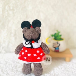K&ouml;nnte beinhalten: Ein handgefertigter brauner Teddyb&auml;r mit einem roten Kleid mit wei&szlig;en Punkten, einem wei&szlig;en Kragen und einem schwarzen Hut mit gro&szlig;en schwarzen Ohren. Der B&auml;r hat eine rote Schleife und den Text "MIRA'S COTTON FRIENDS".