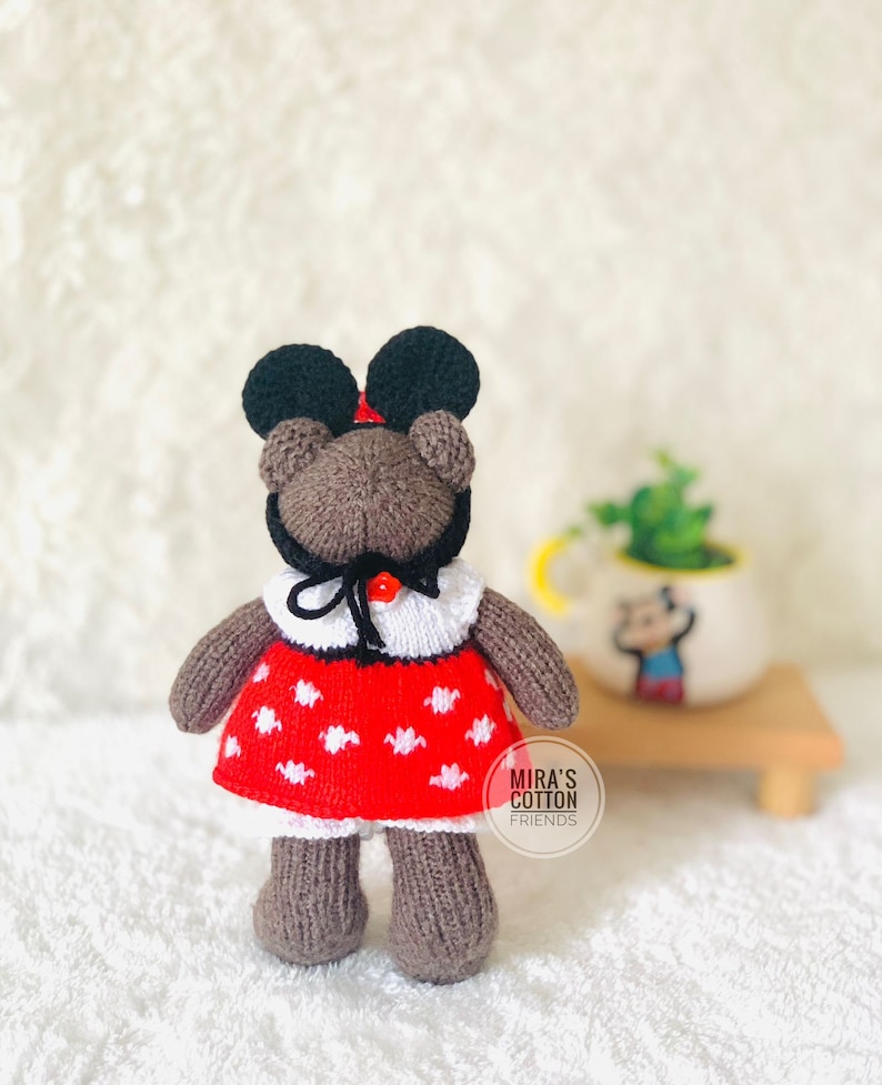 K&ouml;nnte beinhalten: Ein handgefertigter brauner Teddyb&auml;r mit einem roten Kleid mit wei&szlig;en Punkten, einem wei&szlig;en Kragen und einem schwarzen Hut mit gro&szlig;en schwarzen Ohren. Der B&auml;r hat eine rote Schleife und den Text "MIRA'S COTTON FRIENDS".