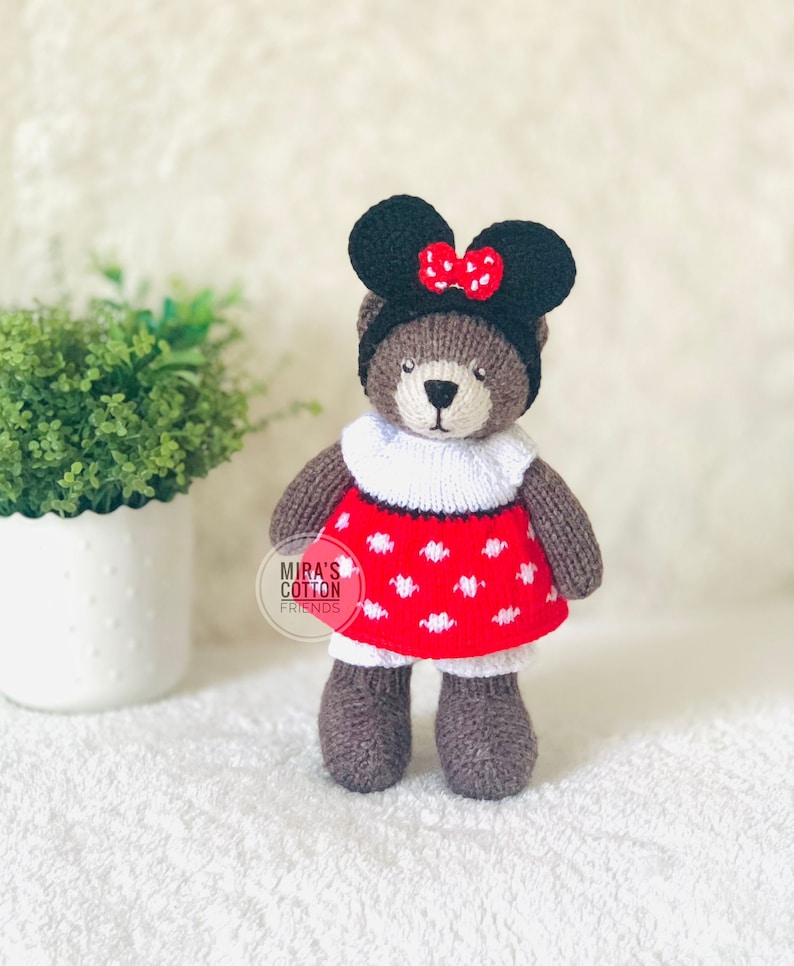 K&ouml;nnte beinhalten: Ein handgefertigter brauner Teddyb&auml;r mit einem schwarzen Stirnband mit M&auml;useohren und einer roten Schleife. Der B&auml;r tr&auml;gt ein rotes Kleid mit wei&szlig;en Punkten und einen wei&szlig;en Kragen. Der Text "Mira's Cotton Friends" ist sichtbar.