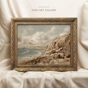 May include: A framed landscape painting of a coastal scene with a rocky cliff, beach, and ocean under a cloudy sky. The ornate gold frame surrounds the artwork. The text "MEDUSA NISH ART GALLERY" is at the top.