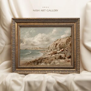 May include: A framed landscape painting of a coastal scene with a beach, cliffs, and ocean under a cloudy sky. The painting is in a gold ornate frame. The text "EROS NISH ART GALLERY" is in the top left corner.