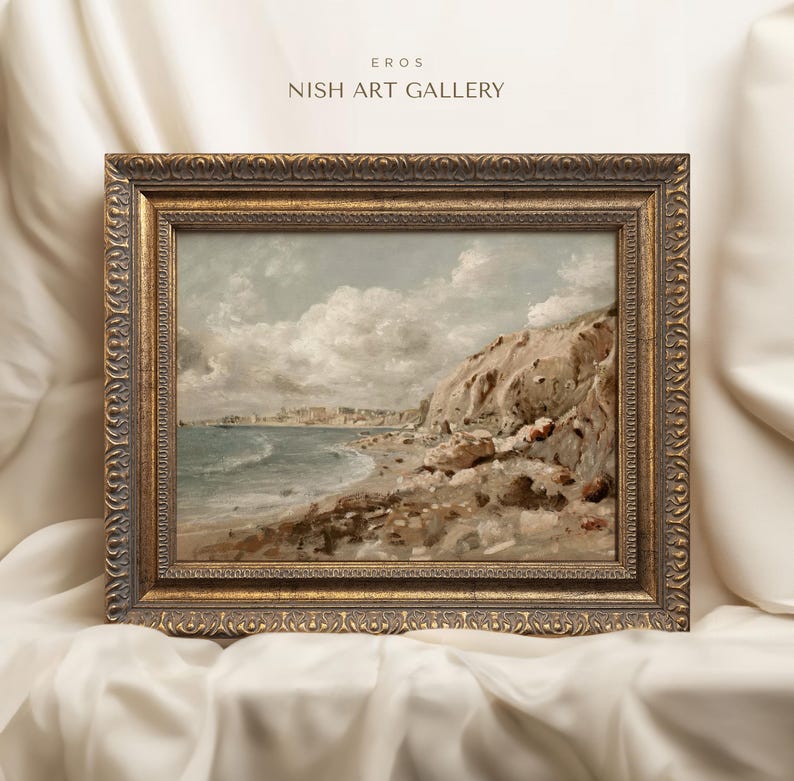 May include: A framed landscape painting of a coastal scene with a beach, cliffs, and ocean under a cloudy sky. The painting is in a gold ornate frame. The text "EROS NISH ART GALLERY" is in the top left corner.